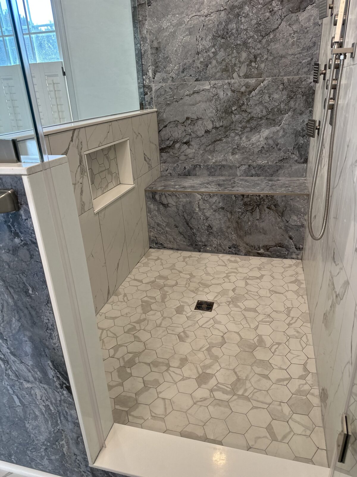Inside walk-in shower with marble bench, hex tile floor, and body sprays